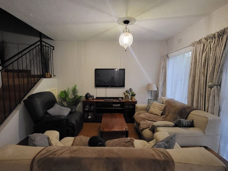 A living room featuring tiled flooring, a staircase with a wrought iron balustrade, and large windows with curtains.