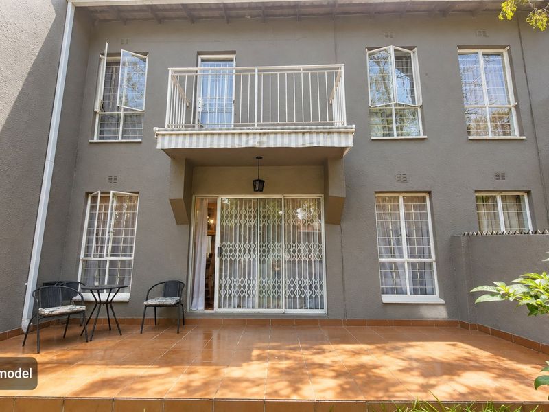 Rear view of the townhouse featuring a tiled patio, a first-floor balcony, and secure metal security gates and window bars.