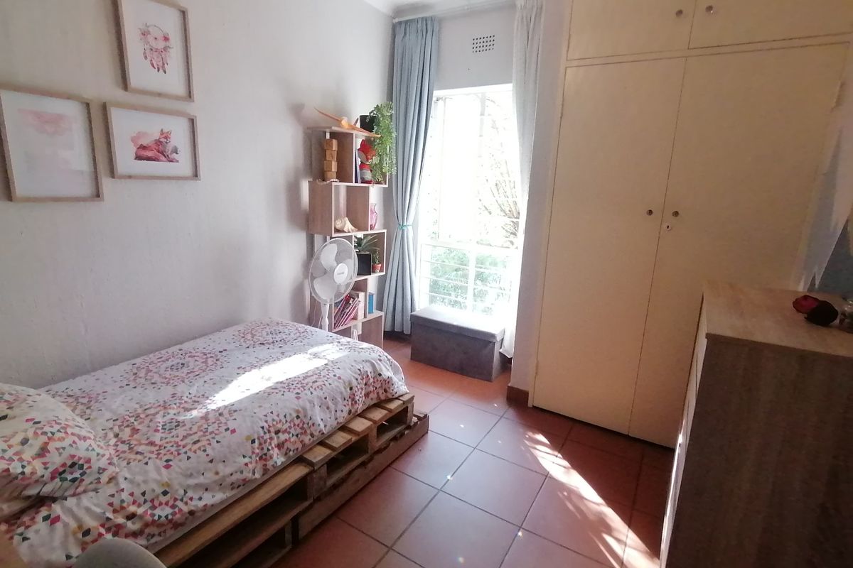 A bedroom featuring tiled flooring, a built-in wardrobe, and a window with security bars, providing natural light.