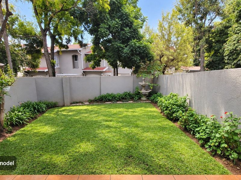 A private, well-maintained rear garden featuring a lush green lawn, established garden beds, and a decorative stone fountain enclosed by a perimeter wall.