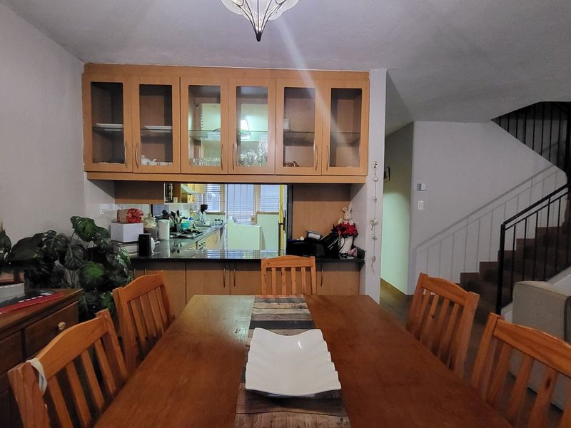 Open plan dining area featuring built-in kitchen cabinetry and a staircase with a metal railing leading to the upper level.