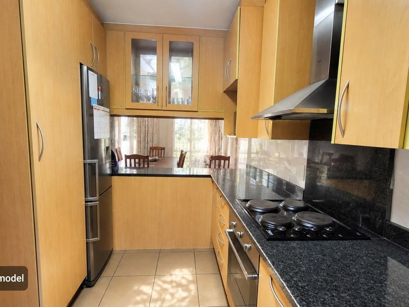 A functional galley-style kitchen featuring light wood cabinetry, dark granite countertops, a built-in oven, and an electric hob with an extractor fan.