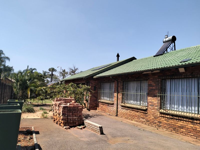 Rear view of a face brick house featuring a green tiled roof, solar water heating system, and security bars on the windows.