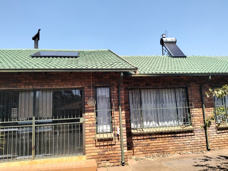 Rear exterior view of a brick house featuring a tiled roof, solar water heating system, solar panels, and security bars on windows.