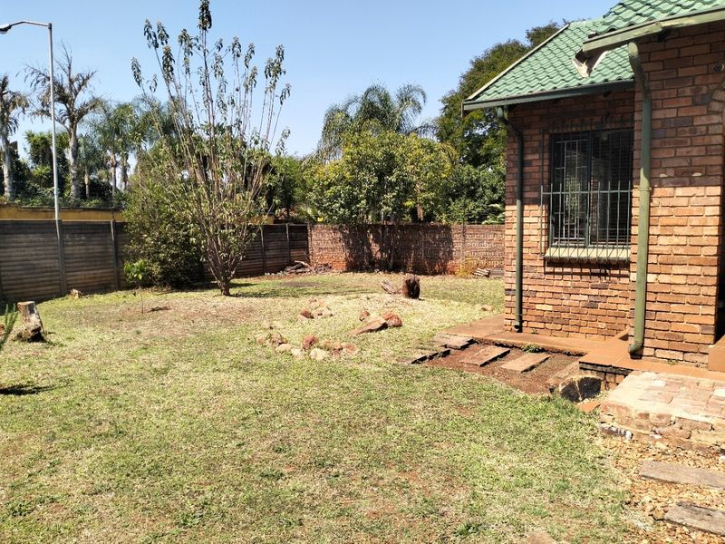 Rear garden area featuring a face brick exterior, security bars on windows, and a precast concrete boundary wall with lawn space.