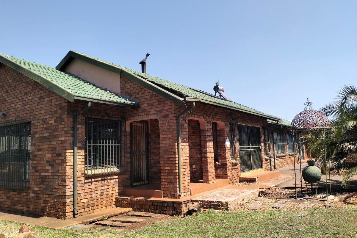 Rear view of a face brick house featuring a green tiled roof, solar water heater, and a covered patio area with security bars.