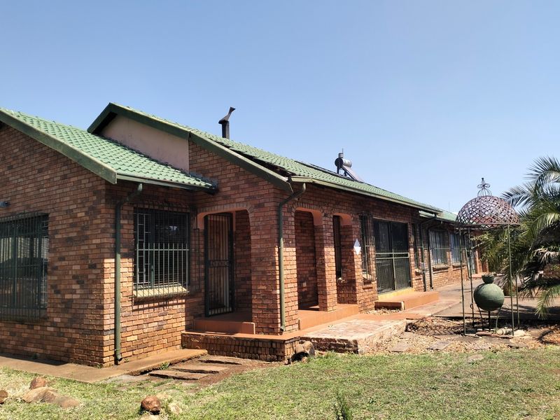Rear view of a face brick house featuring a green tiled roof, solar water heater, and a covered patio area with security bars.