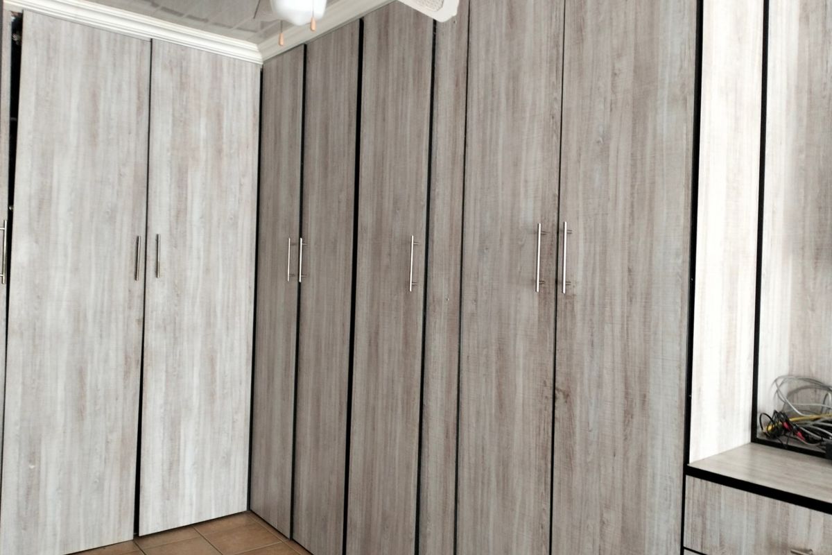 A bedroom featuring extensive built-in cupboards with a modern wood-grain finish, tiled flooring, and a ceiling fan.