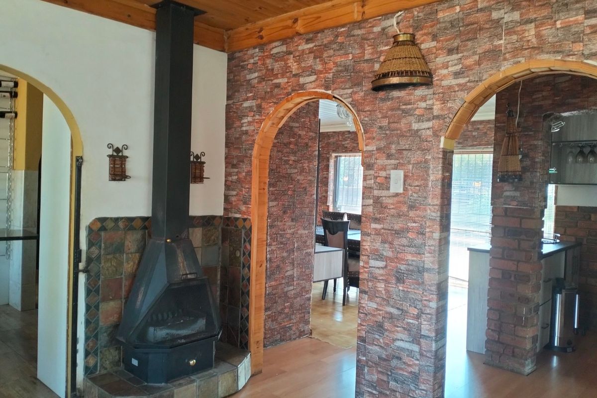 Living area featuring a freestanding fireplace with tiled hearth, timber ceiling, and arched doorways leading to adjacent spaces with brick-effect wall finishes.