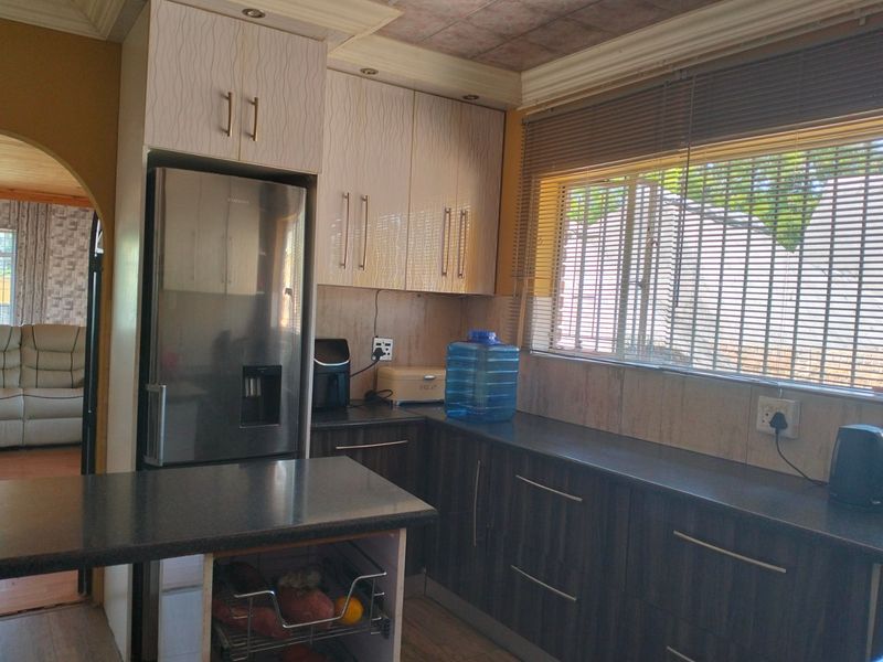 A functional kitchen featuring two-tone cabinetry, dark laminate countertops, and a window with fitted blinds, offering a practical layout for daily use.