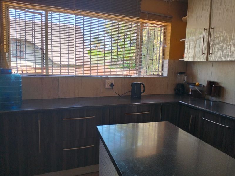 A functional kitchen featuring dark laminate cabinetry, stone countertops, and a central island, illuminated by natural light through large windows.