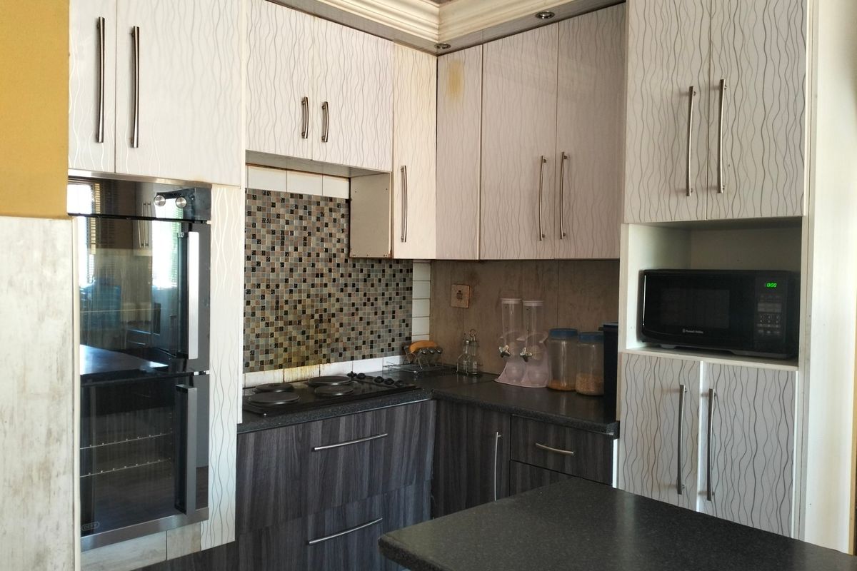 Compact kitchen featuring modern laminate cabinetry, mosaic tile backsplash, built-in oven, and stone countertops with integrated storage solutions.