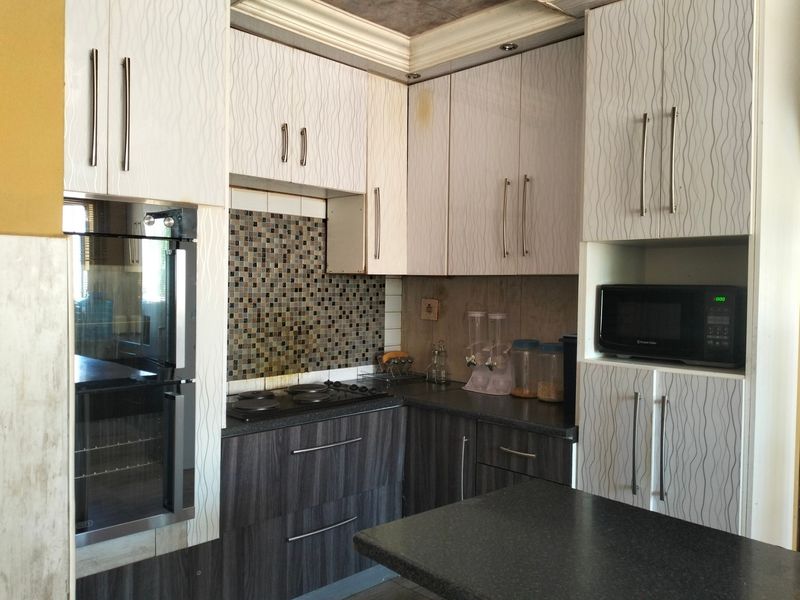 Compact kitchen featuring modern laminate cabinetry, mosaic tile backsplash, built-in oven, and stone countertops with integrated storage solutions.