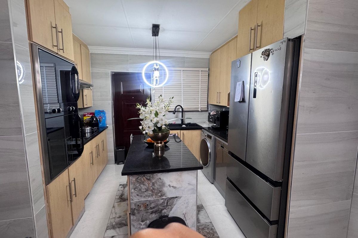 Modern kitchen featuring light wood cabinetry, granite countertops, a central island, and integrated appliances with contemporary finishes.