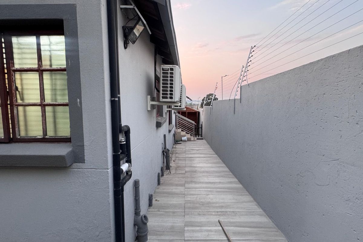 A narrow side walkway featuring tiled flooring, boundary wall with electric fencing, and an external air conditioning unit.
