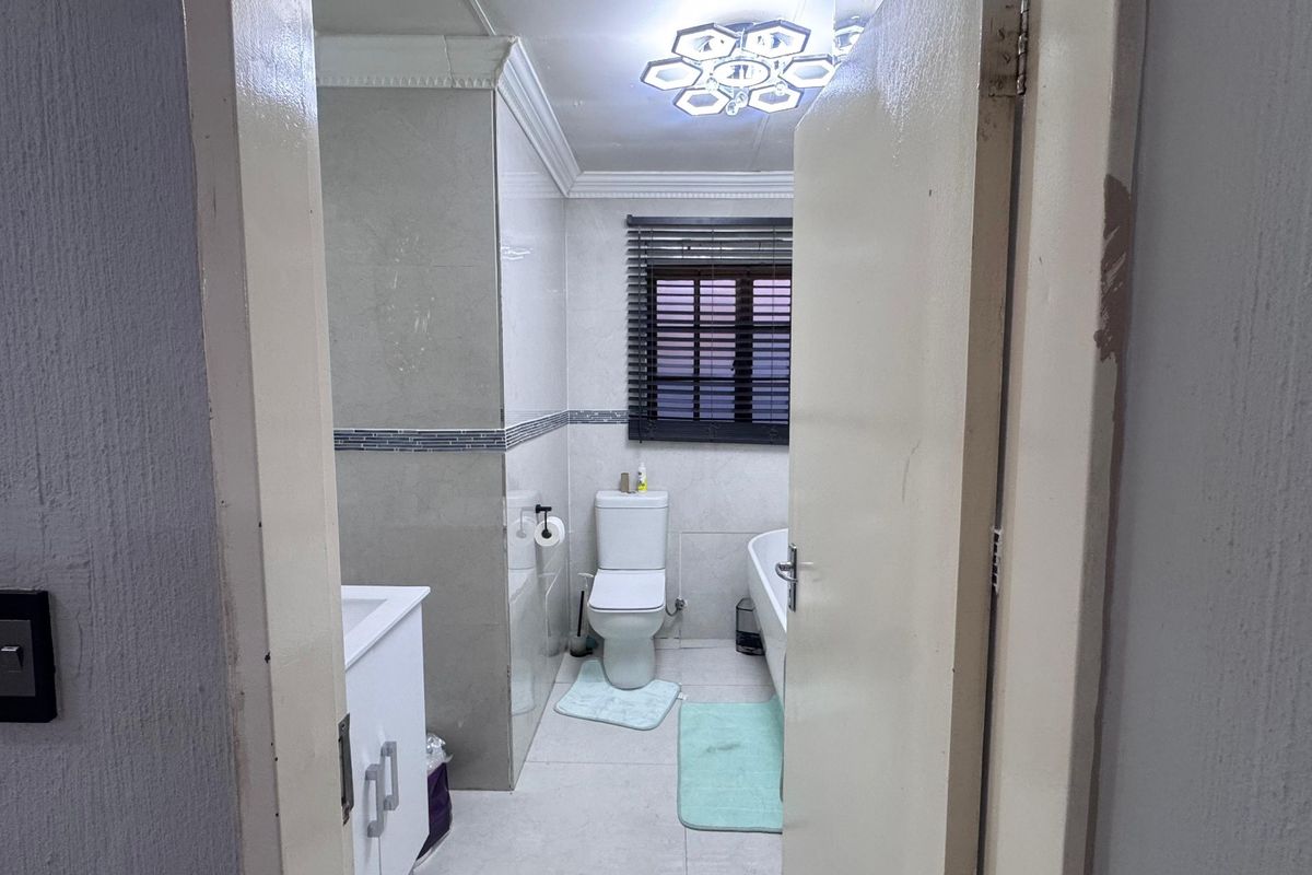 A functional bathroom featuring tiled walls and flooring, a vanity, a toilet, and a bathtub, illuminated by a modern ceiling light fixture.