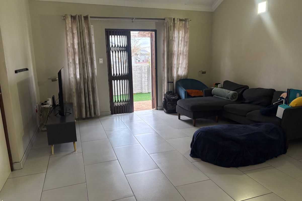Spacious living room featuring large format floor tiles, a vaulted ceiling, and direct access to an outdoor area through a secure sliding door.