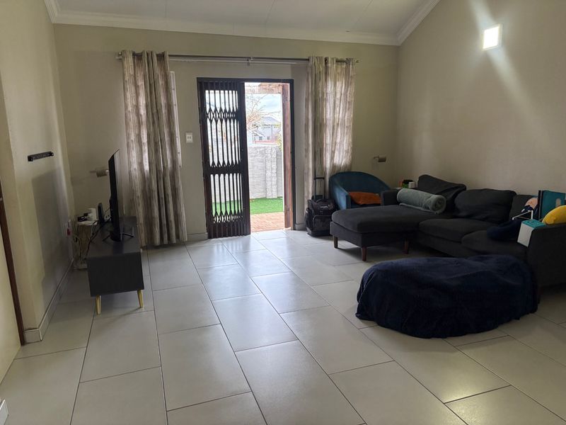 Spacious living room featuring large format floor tiles, a vaulted ceiling, and direct access to an outdoor area through a secure sliding door.