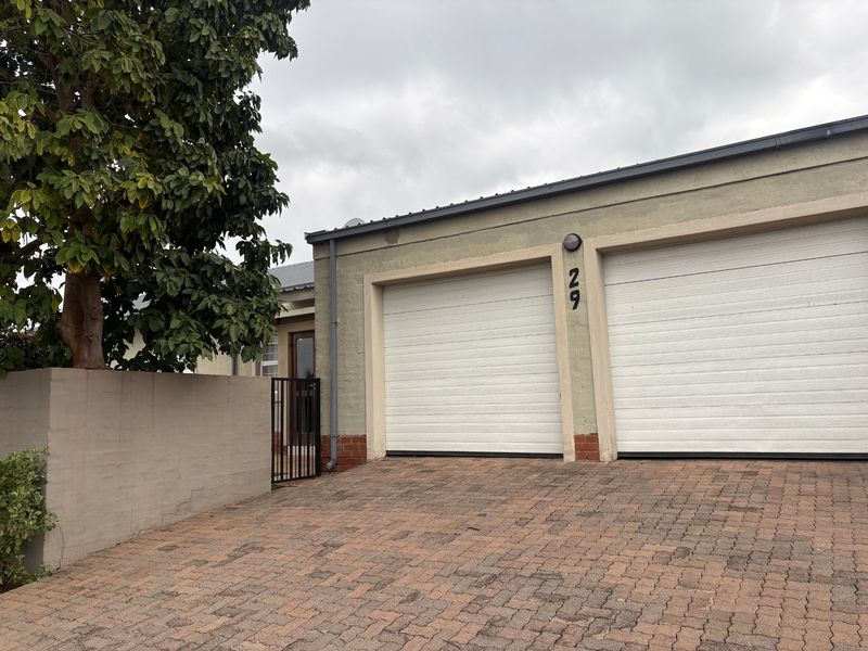 Front exterior view of a cluster home featuring a double garage, paved driveway, and a private gated entrance.