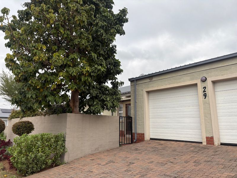 Front elevation of a cluster home featuring a double garage, paved driveway, and a private pedestrian entrance with a boundary wall.