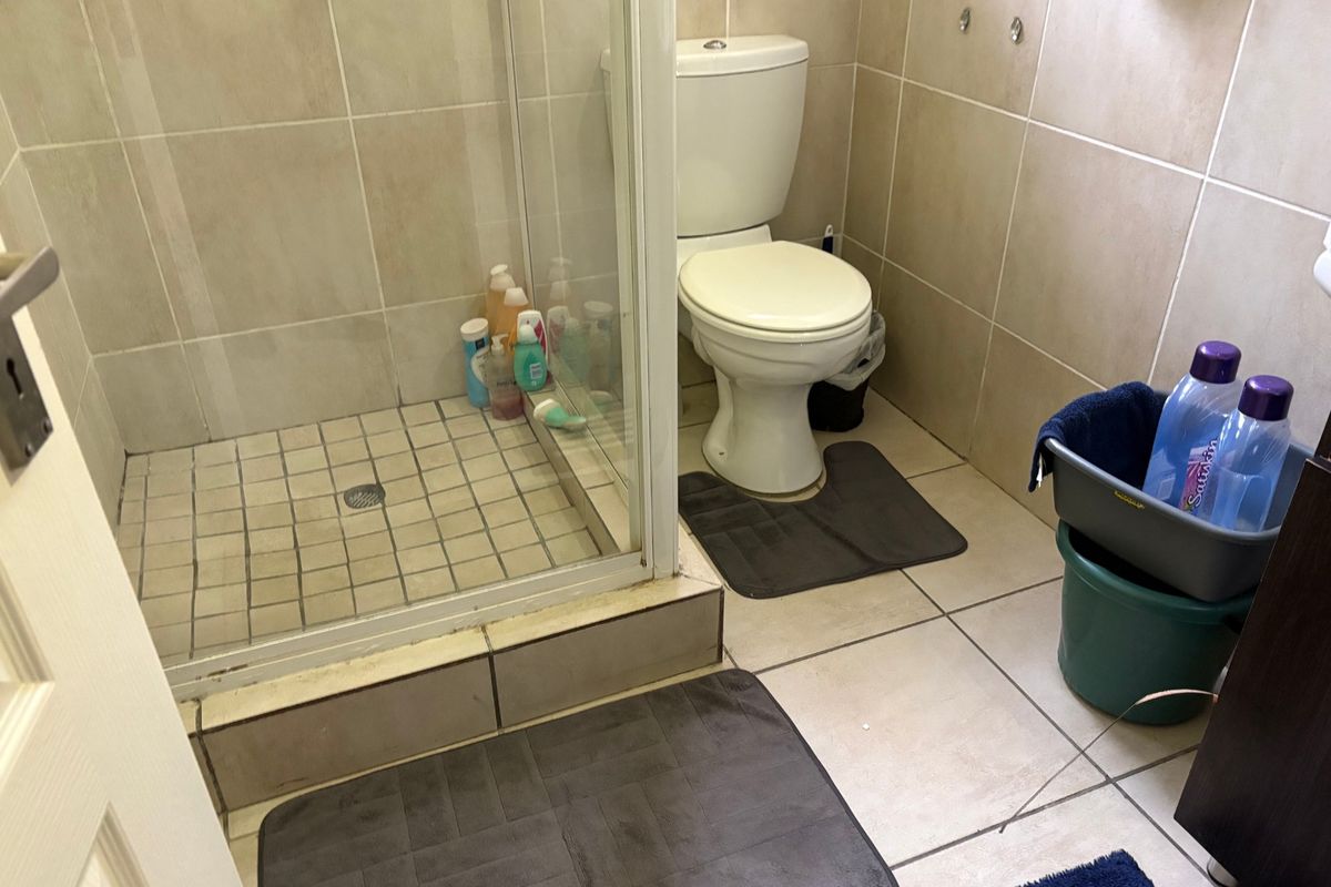 A functional bathroom featuring a glass-enclosed shower and standard toilet with neutral ceramic wall and floor tiling.