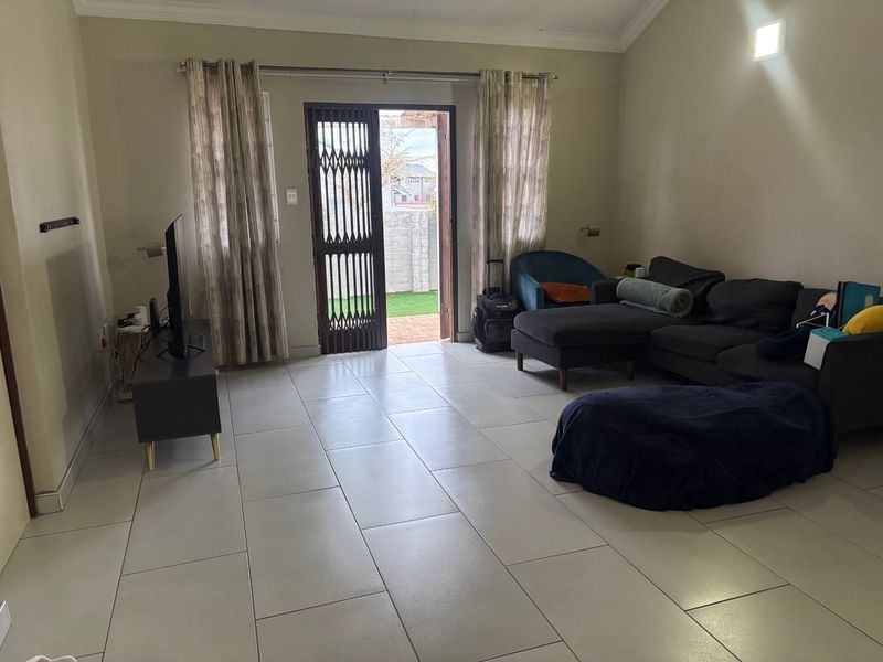 A spacious living room featuring neutral tiled flooring, coved ceilings, and direct access to an outdoor area through a secure sliding door.