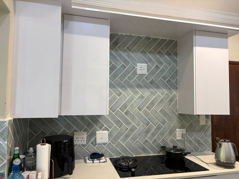 Modern kitchen area featuring white cabinetry, a stylish herringbone tile backsplash, and a sleek built-in electric hob set into a stone countertop.