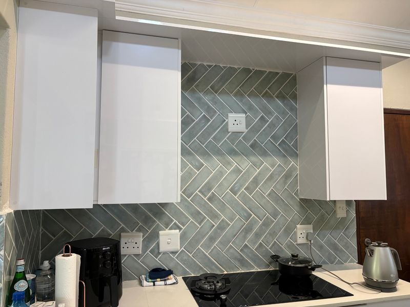 Modern kitchen area featuring white cabinetry and a stylish grey herringbone tile backsplash with a built-in electric hob.
