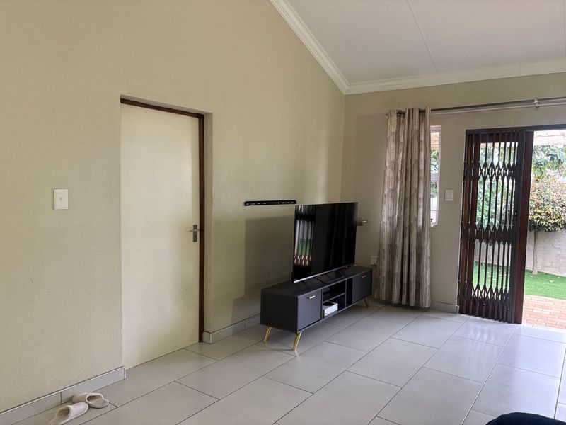 A living room featuring tiled flooring, a vaulted ceiling, and a security gate leading to the outdoor area.