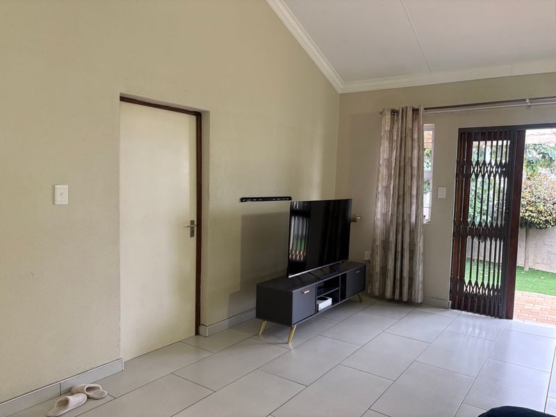 A living room featuring tiled flooring, a vaulted ceiling with cornice detailing, and a security gate providing access to the outdoor area.