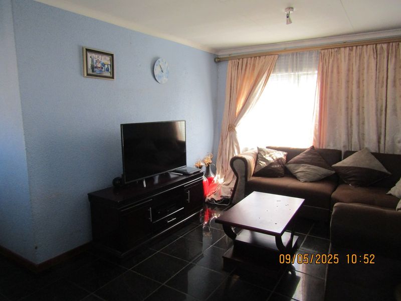 A living room featuring dark tiled flooring and natural light from a window with curtain rails.