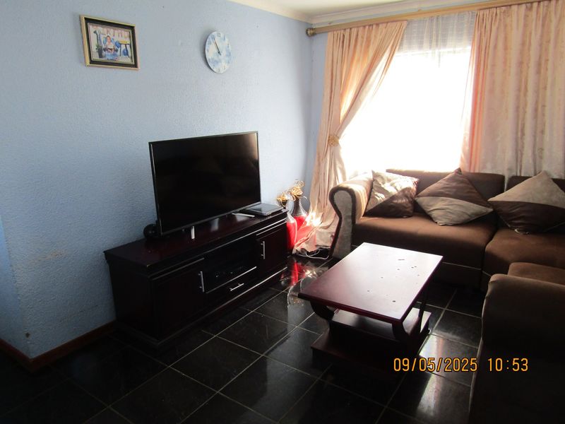 A living room area featuring dark tiled flooring and natural light from a window with curtain rails.