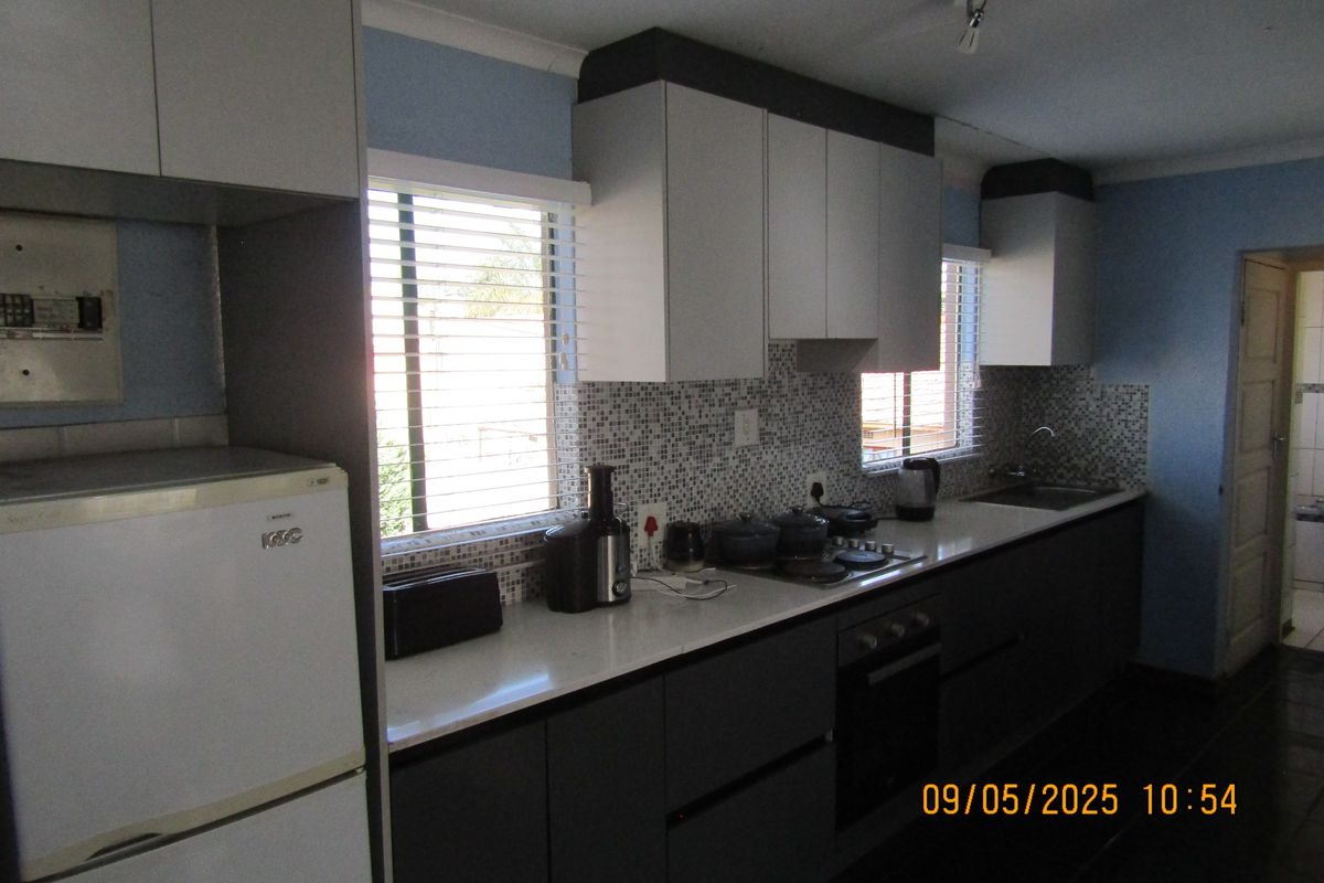A functional kitchen featuring two-tone cabinetry, mosaic tile backsplash, integrated electric hob, built-in oven, and a stainless steel sink.