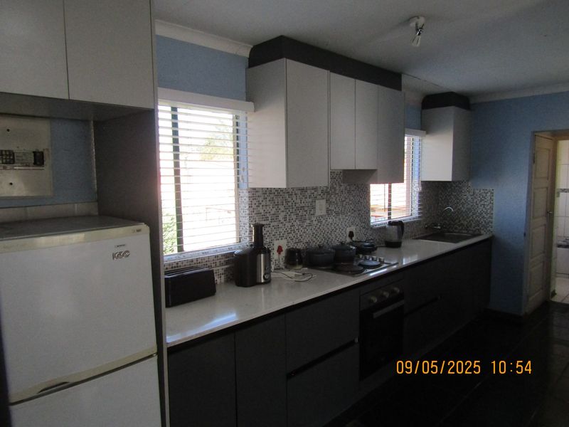 A functional kitchen featuring two-tone cabinetry, mosaic tile backsplash, integrated electric hob, built-in oven, and a stainless steel sink.