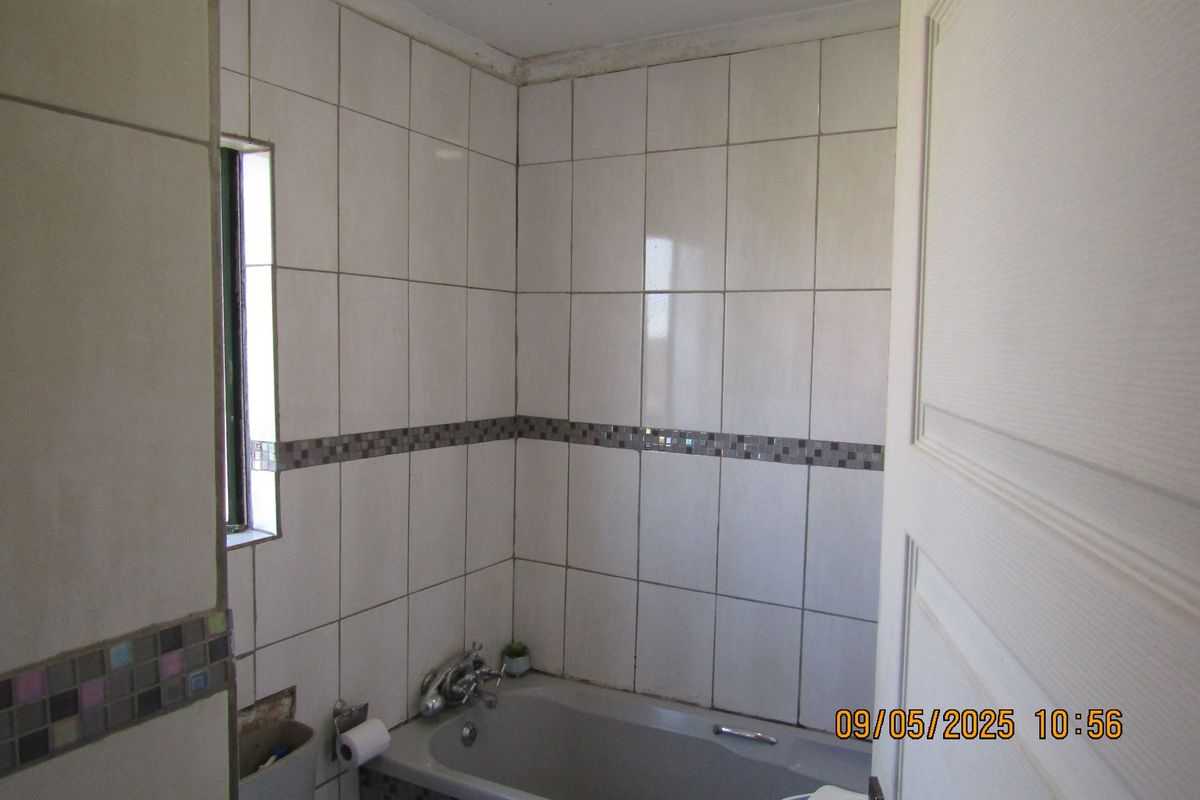 A small bathroom featuring a bathtub with tiled walls and a decorative mosaic border, currently showing signs of wear and missing tile work.