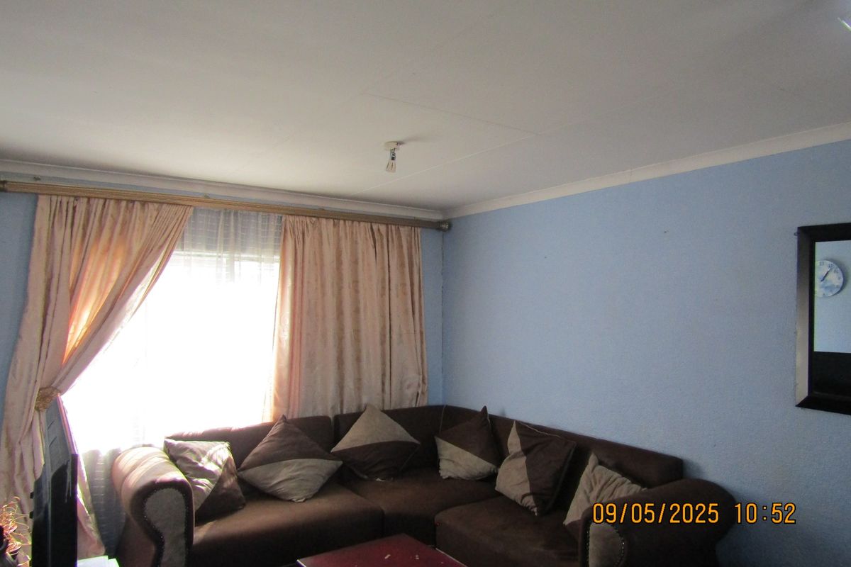 A living room featuring blue walls, coving, and a window with curtain rods. The space requires cosmetic updates to improve its overall appeal.