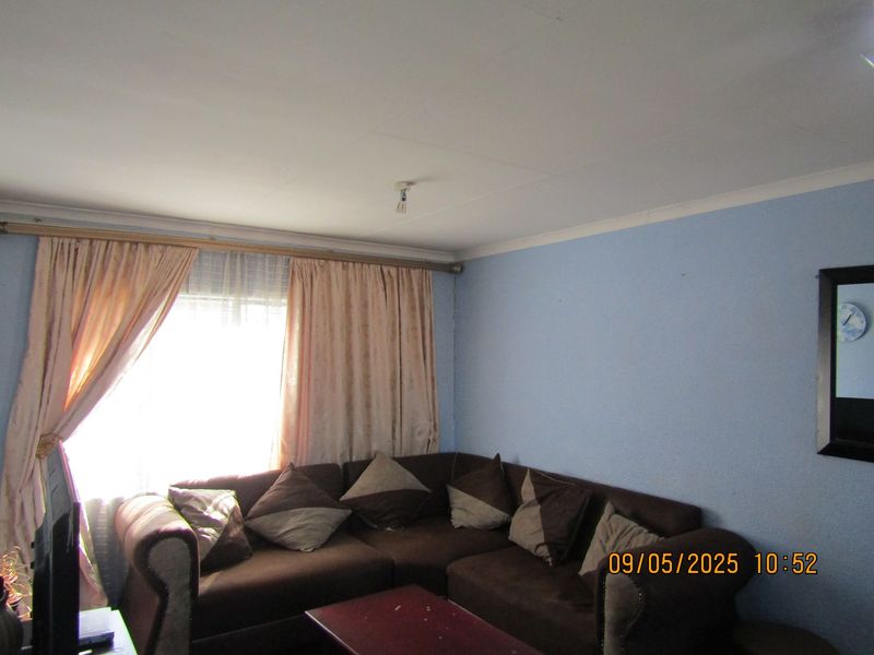 A living room featuring blue walls, coving, and a window with curtain rods. The space requires cosmetic updates to improve its overall appeal.