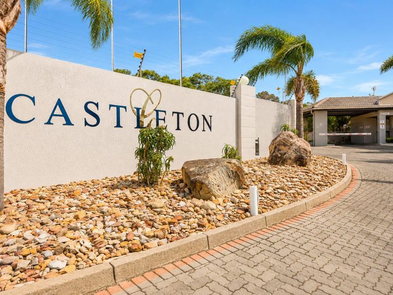 The entrance to Castleton complex featuring a secure boundary wall, electric fencing, and a paved driveway with a security boom gate.