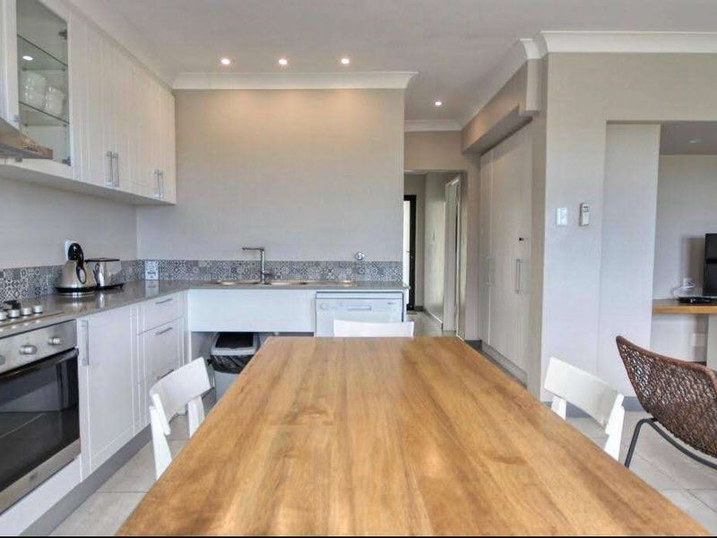 Modern open-plan kitchen and living area featuring sleek white cabinetry, gas hob, integrated oven, and stylish tiled backsplash with neutral finishes throughout.