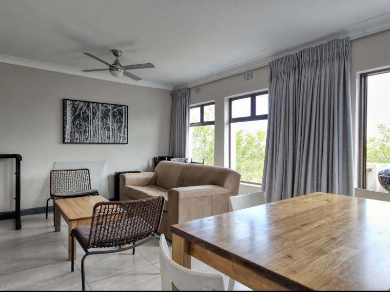 Spacious open-plan living and dining area featuring neutral tiled flooring, a ceiling fan, and large windows providing natural light with access to a balcony.