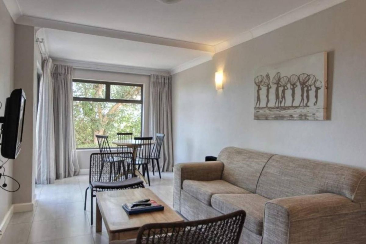 A neutrally painted living room featuring tiled flooring, coving, and a large window providing natural light.