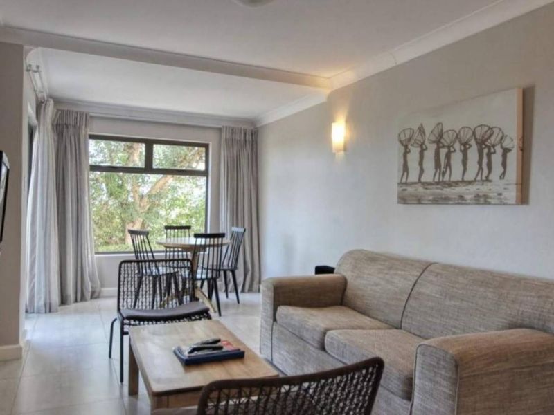 A neutrally painted living room featuring tiled flooring, coving, and a large window providing natural light.