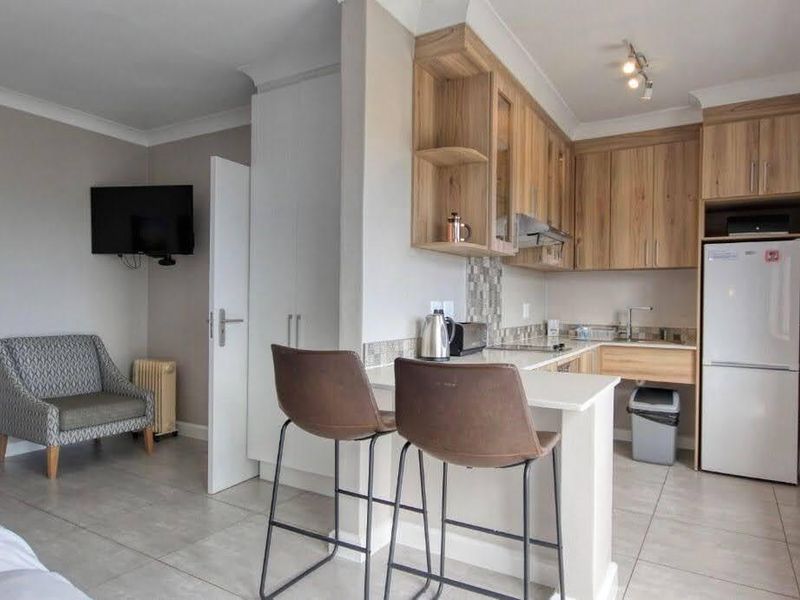 An open-plan living area featuring a modern kitchen with light wood cabinetry, stone countertops, and tiled flooring, seamlessly connected to a cozy lounge space.