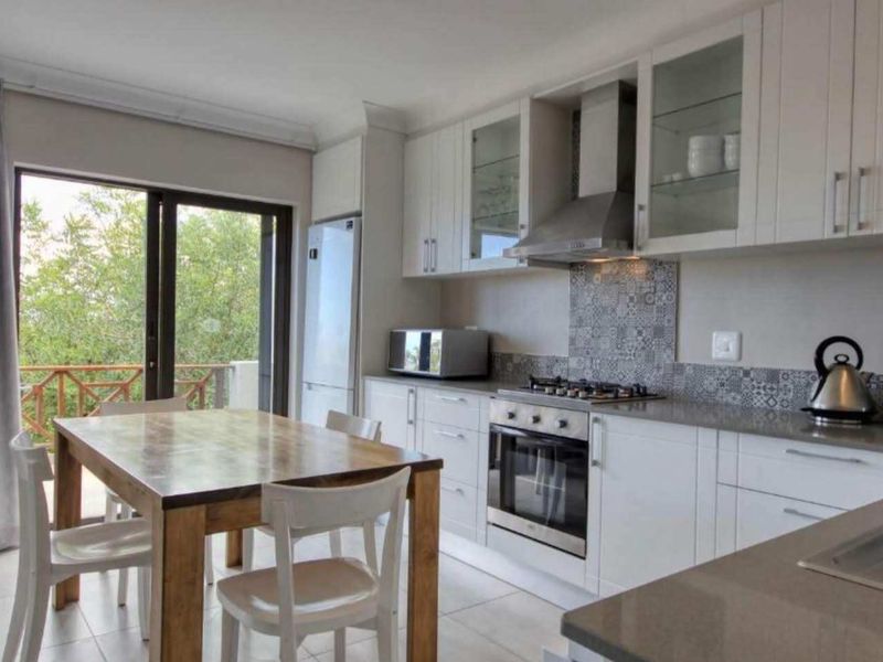 Modern open-plan kitchen and dining area featuring white cabinetry, stone countertops, integrated appliances, and direct access to a balcony through sliding glass doors.