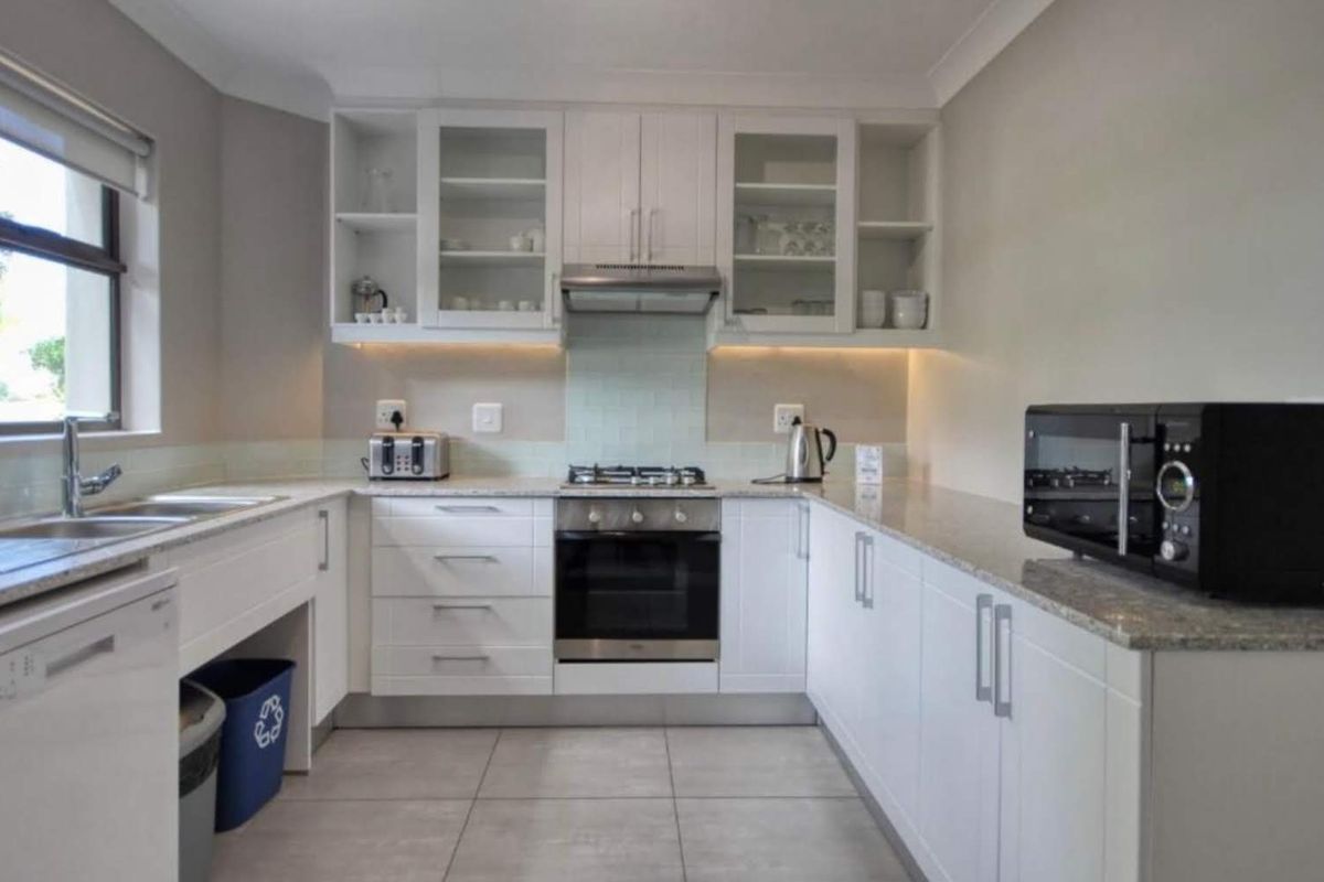 Modern kitchen featuring white cabinetry, granite countertops, built-in oven, gas hob, extractor fan, and tiled flooring with ample storage space.