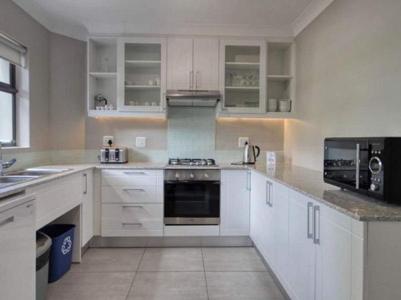 Modern kitchen featuring white cabinetry, granite countertops, built-in oven, gas hob, extractor fan, and tiled flooring with ample storage space.