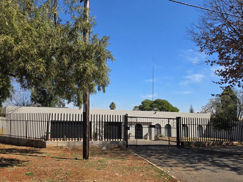 Front exterior view of the property featuring a secure perimeter fence, gated driveway access, and a single-story building facade with security shutters.
