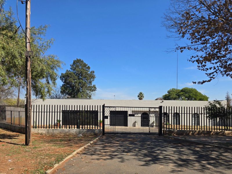 Front elevation of a single-story residence featuring a secure metal perimeter fence, gated driveway entrance, and a stucco facade.