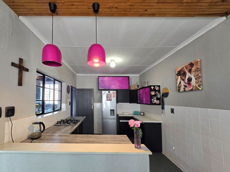 A functional kitchen featuring dark cabinetry, a gas hob, laminate countertops, and a timber-paneled ceiling with vibrant pendant lighting.