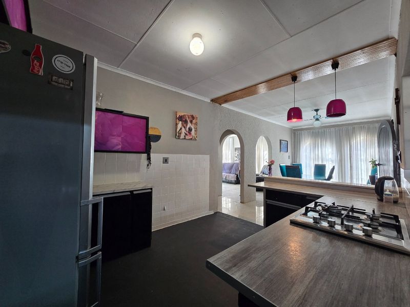 Open-plan kitchen and dining area featuring a gas hob, tiled splashback, distinctive archways, and pendant lighting, offering a functional layout with potential for modernization.